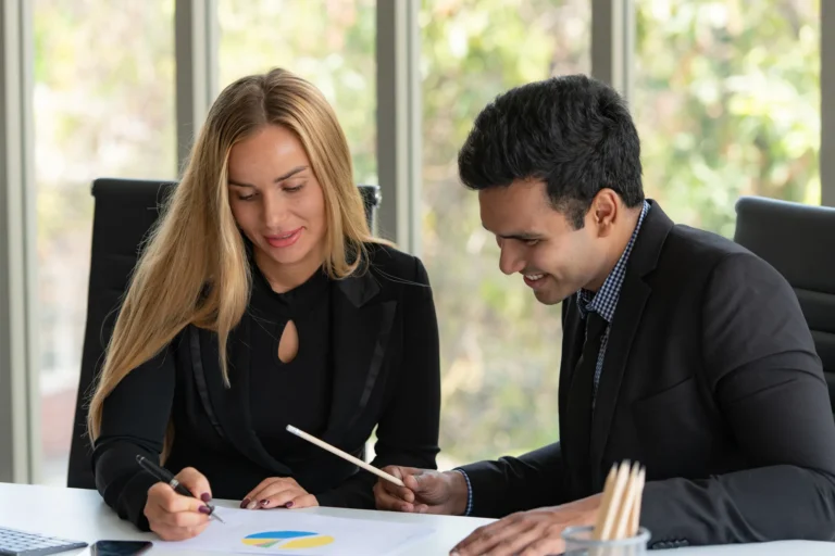 Un hombre y una mujer revisan un gráfico en una mesa de trabajo parte del servicio de empresas de coaching empresarial en México.