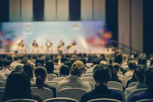 Un coach empresarial en un escenario frente a una gran audiencia sentada en un auditorio durante una conferencia.