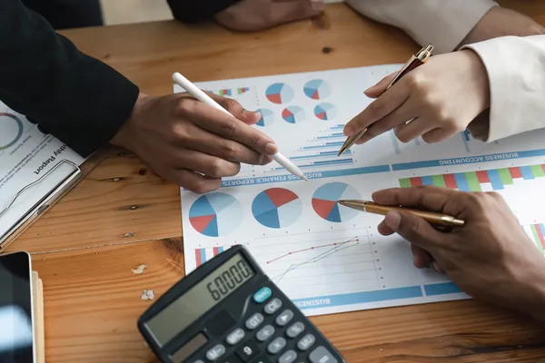 Un equipo revisa informes financieros con gráficos circulares y una calculadora para saber como aumentar las ventas en mi negocio.