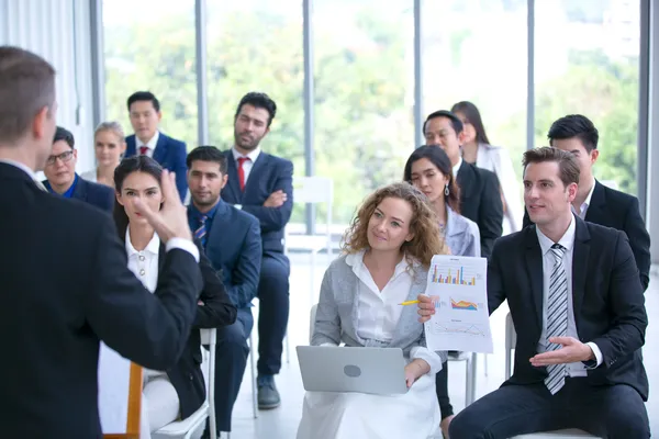 Audiencia interactúa con ponente; un hombre gesticula y una mujer muestra gráficos en conferencias de coaching empresarial.